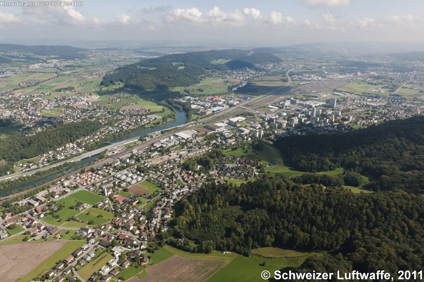 Limmat-Tal, Blickrichtung SE. Im Limmatknie links: Würenlos und Blick ins Furttal (rechts im Bild oben), rechts in der Limmatschleife: Industriegebiet 'Neuhard'. Rangierbahnhof Limmattal, davor (mit Hochhäusern): Spreitenbach. Rechts am Bildrand oben: Dietikon.